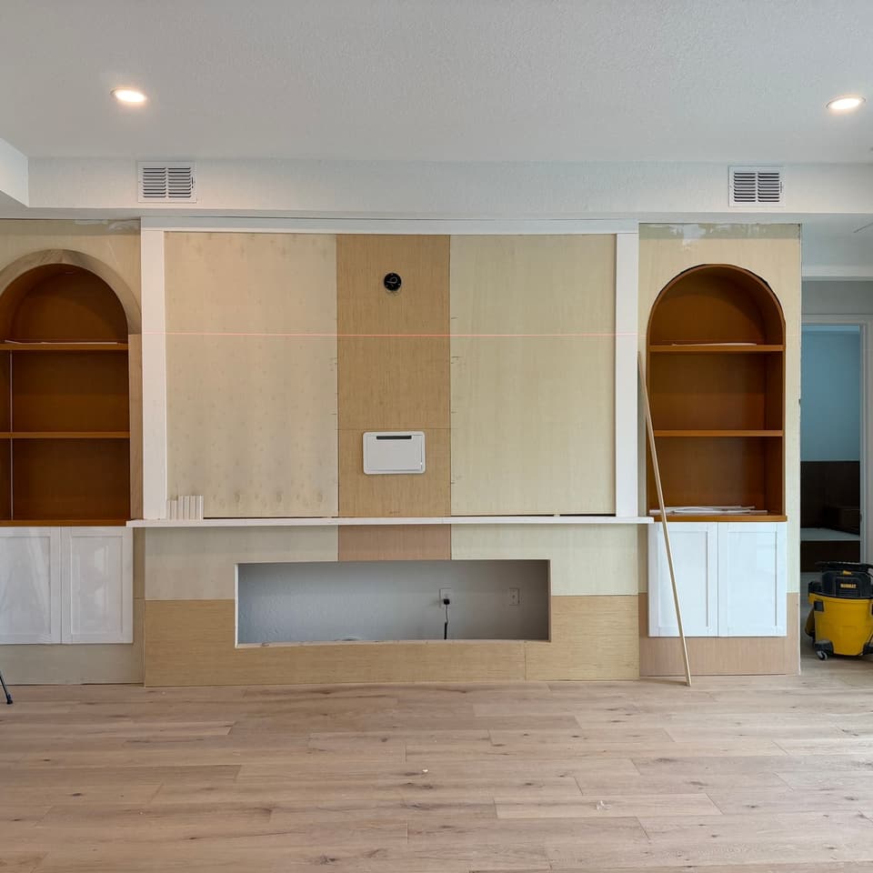 Mueble de pared en construcción: nichos arqueados y hueco de chimenea armados en tablero, con gabinetes imprimados y las herramientas aún en obra
