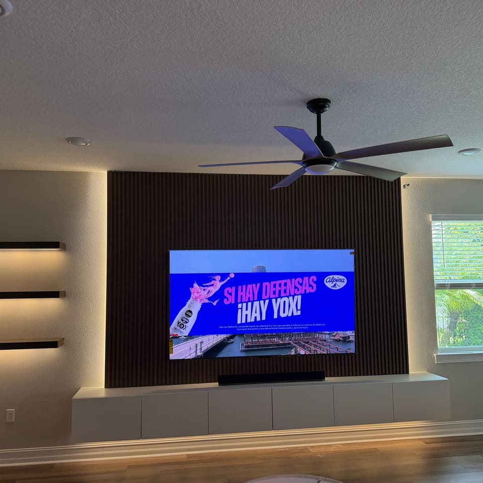 Sala con pared decorativa de listones de madera oscura, televisor montado, tres estantes flotantes con iluminación oculta y mueble multimedia empotrado