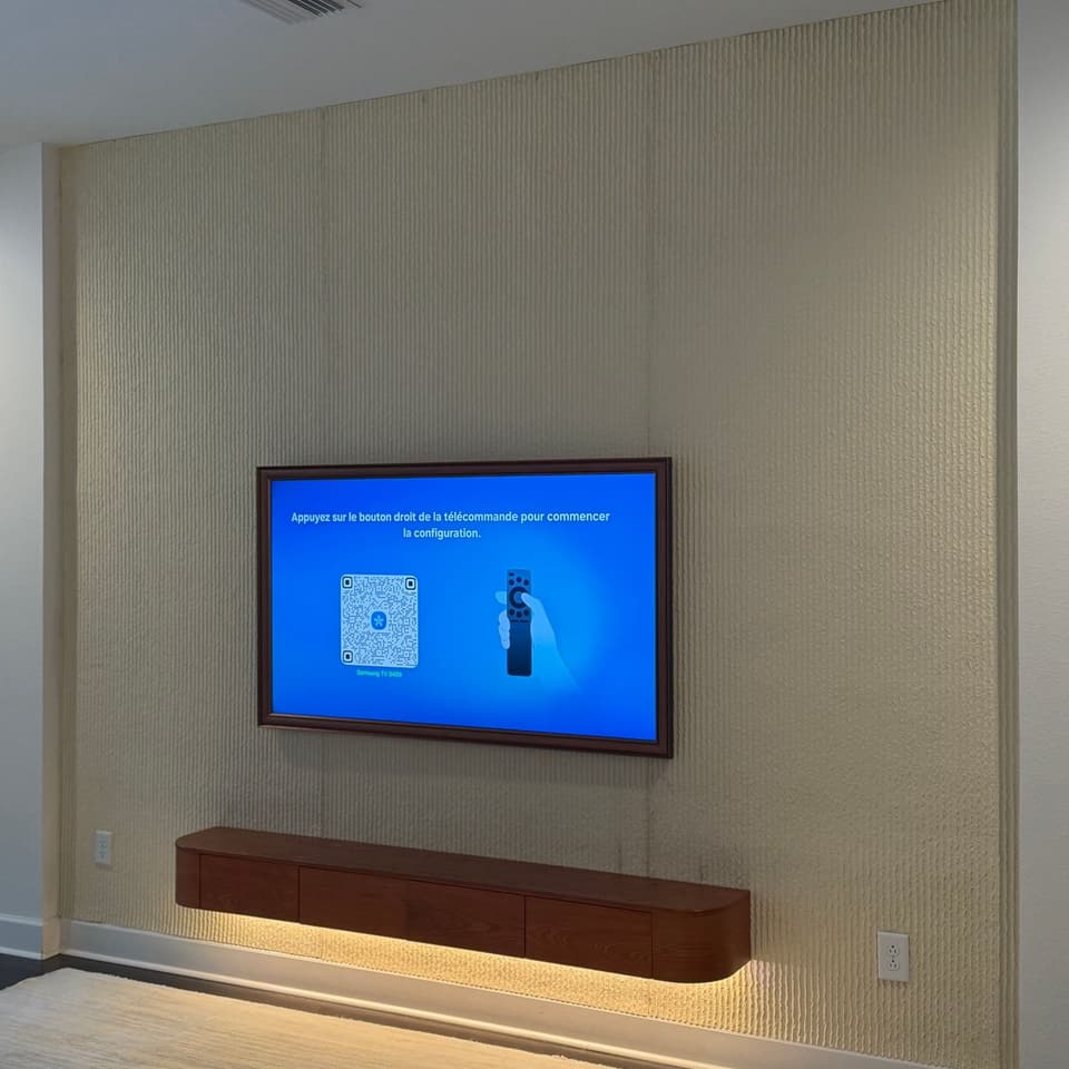 Televisor montado en una pared texturizada sobre una credenza flotante de madera iluminada por debajo