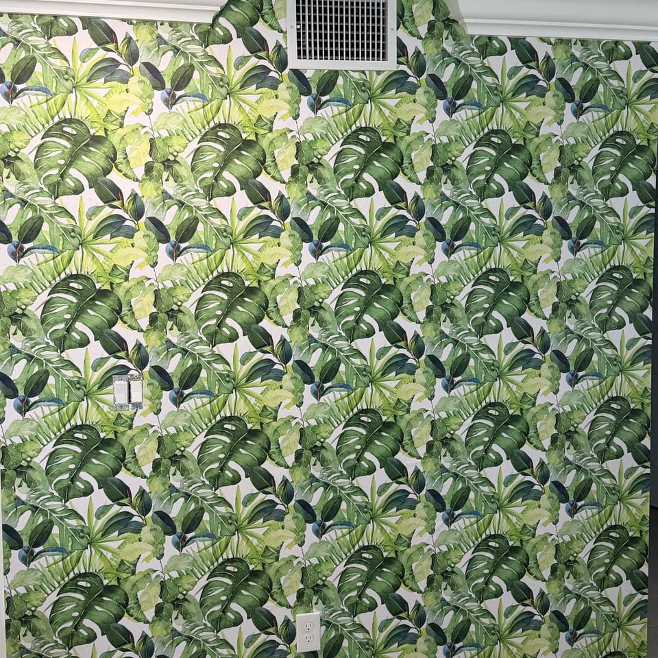 Papel tapiz de hojas tropicales colocado en toda una pared, rematado contra la moldura de corona y el zócalo